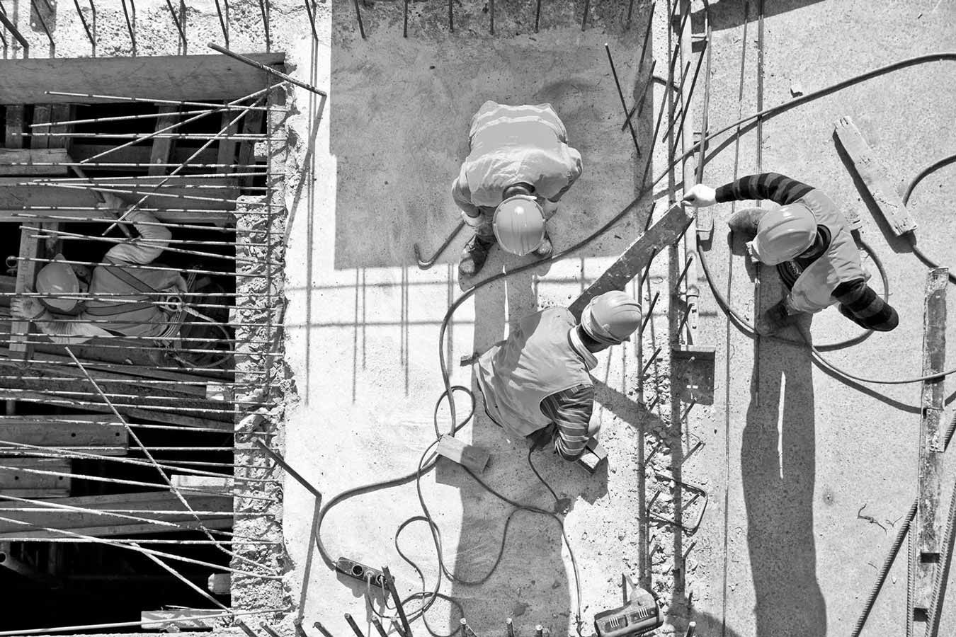 Bild in schwarz und weiß, das Bauarbeiter auf einem Rohbau aus der Vogelperspektive zeigt